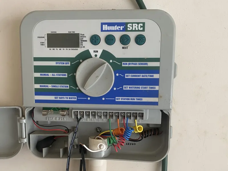Hunter SRC sprinkler controller with its door open, showing the dial settings and colored zone wires connected to the terminal strip