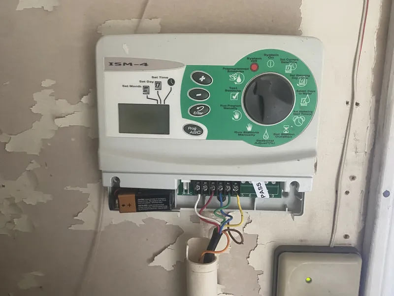 ISM-4 sprinkler controller with a blank display and its wiring cover off, showing a battery and connected zone wires