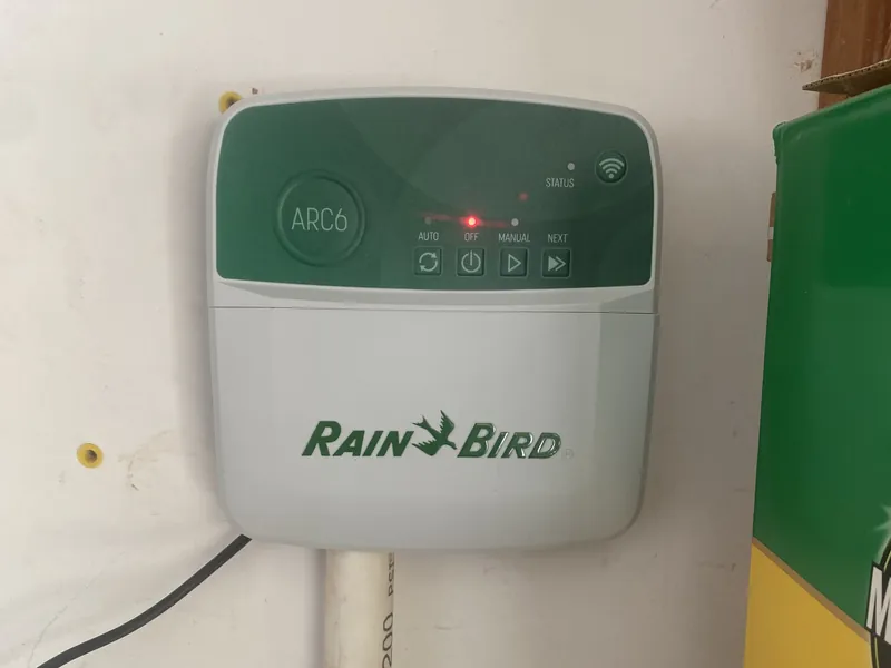 Rain Bird ARC6 sprinkler controller with a red light lit above its Auto, Off, Manual and Next buttons, mounted on a wall