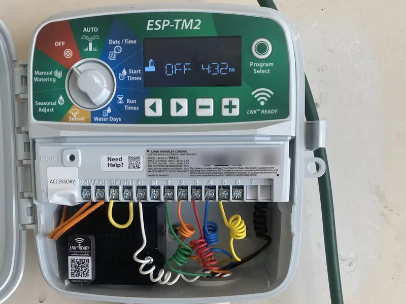 Rain Bird ESP-TM2 sprinkler controller with its door open, showing OFF and 4:32 PM on the display and color-coded zone wires on the terminals