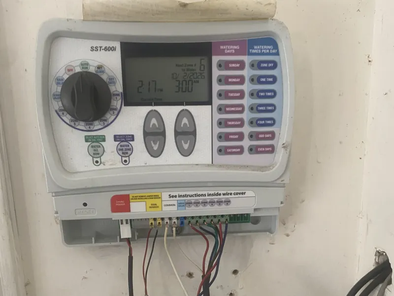 SST-600i sprinkler timer with a dial, LCD screen and watering-day buttons, with colored zone wires connected to its terminals