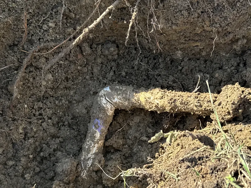Dirt-covered PVC pipe elbow exposed in a hole dug in the soil