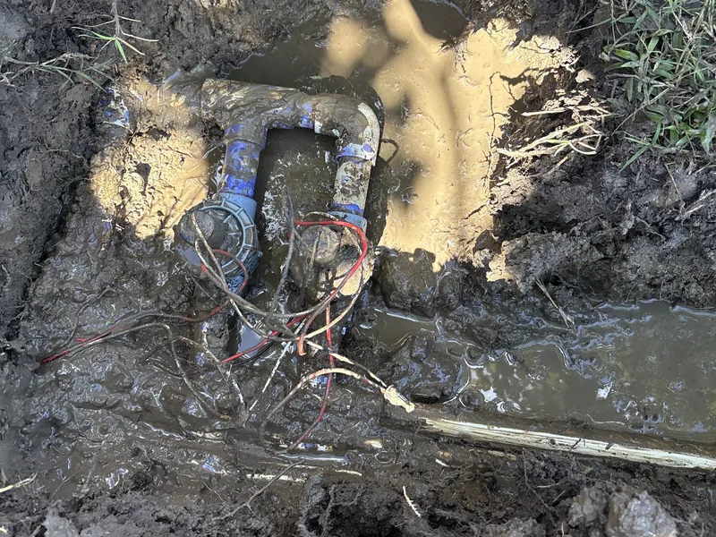 Sprinkler valves on a PVC manifold sitting in muddy water in an open hole